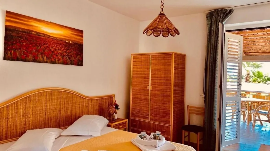 Camera in stile mediterraneo con letto, armadio in vimini, quadro decorativo e accesso al balcone