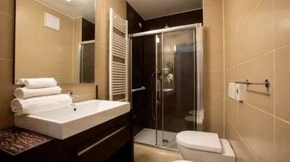 Bagno moderno con lavabo, specchio grande, doccia con parete in vetro e set di asciugamani bianchi piegati.