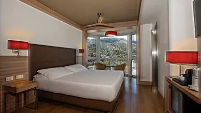 Camera d'hotel moderna con letto matrimoniale, terrazza panoramica con vista su montagne e due poltrone.