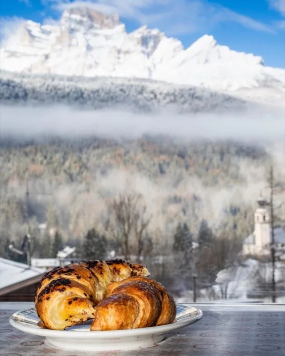 Cornetti su un piatto vicino a una finestra con panorama di montagne innevate e bosco invernale.