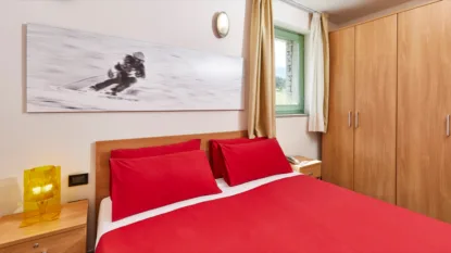 Camera da letto con letto matrimoniale rosso, comodini in legno, armadio e finestra con vista montagna.