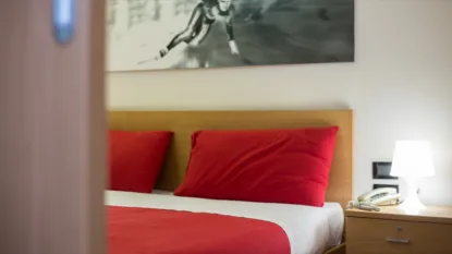 Camera da letto con letto matrimoniale, cuscini e copriletto rossi, lampada accesa e telefono sul comodino.