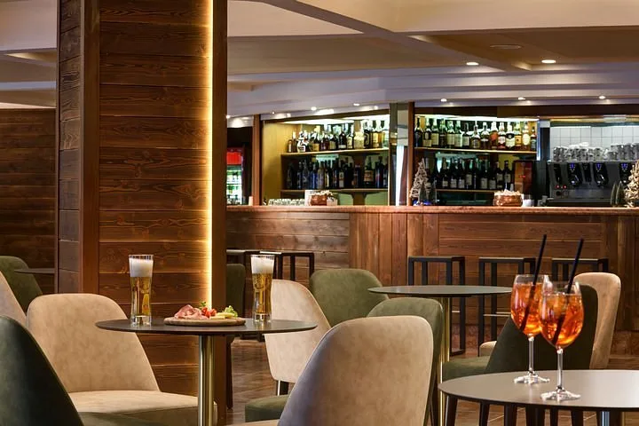 Bar dell'hotel con banco in legno, sgabelli e aperitivi sui tavolini
