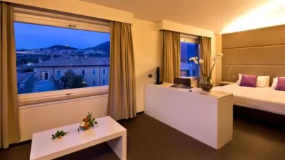 Camera moderna con finestra che offre vista panoramica, arredamento elegante e fiori decorativi su un tavolino.