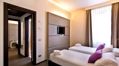 Camera d'albergo moderna con due letti singoli, TV a parete, tende chiare e arredamento elegante.