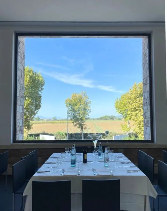 Interno di una sala da pranzo con vista su un paesaggio di campagna e un grande quadro sulla parete con tavolo apparecchiato.