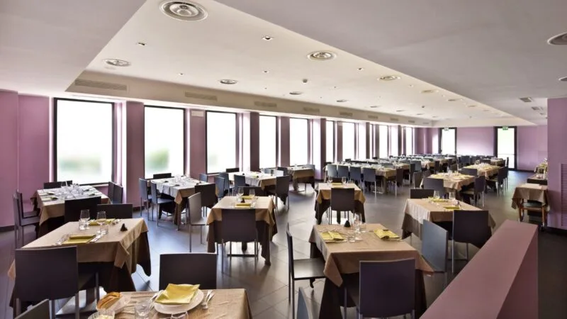 Interno di un ristorante elegante con tavoli ben apparecchiati e finestre ampie che lasciando filtrare la luce.