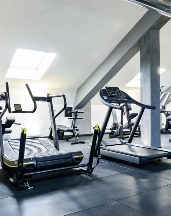 Attrezzature da palestra in un ambiente spazioso con luci naturali e soffitto inclinato.