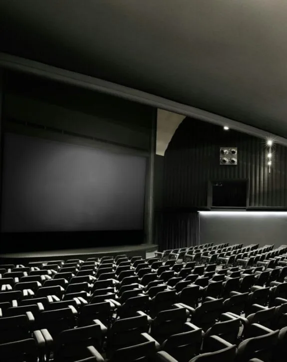 Sala cinematografica vuota con schermo e sedie in primo piano.