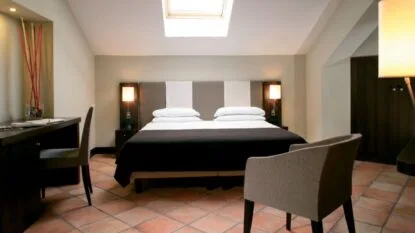 Camera da letto moderna con letto matrimoniale, due lampade morbide, scrivania, poltrone e pavimento in cotto.