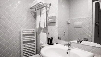 Bagno moderno con piastrelle grigie a rombi, lavabo bianco, specchio e asciugamani bianchi appesi.