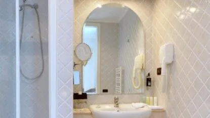 Bagno con lavabo bianco, specchio ad arco, asciugacapelli, doccia con parete in piastrelle beige.