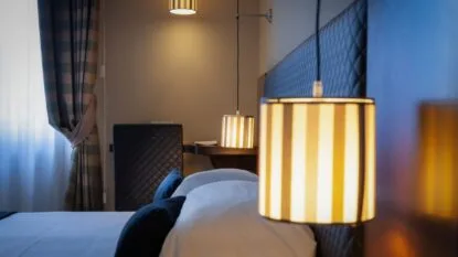 Interno di camera da letto con lampade a sospensione a strisce illuminate, letto con testiera imbottita e tende a righe.