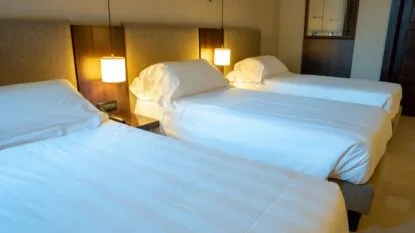 Camera d'albergo con tre letti singoli, testate imbottite e lampade da comodino accese.