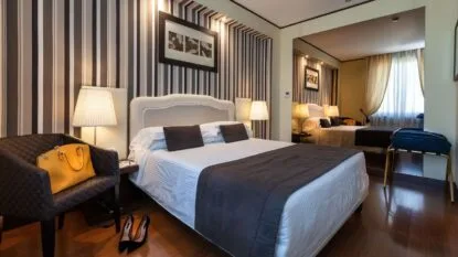 Camera da letto elegante con letto matrimoniale, poltrona con borsa gialla, lampade, specchio grande e pavimento in legno.