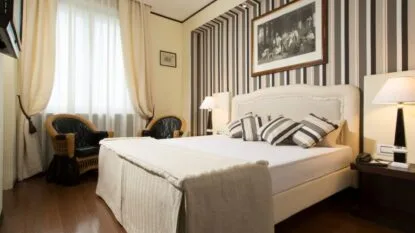 Camera da letto elegante con letto matrimoniale, cuscini a righe, due poltrone in vimini e pareti a strisce verticali.