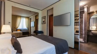 Camera d'albergo moderna con letto matrimoniale, TV a schermo piatto, specchio grande e bagno con doccia in stile industriale.