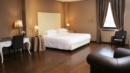 Camera da letto moderna con letto matrimoniale, scrivania, poltrone e pavimento in legno scuro.