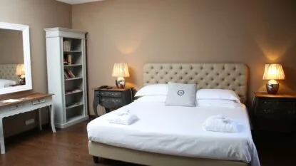 Camera da letto elegante con letto matrimoniale, due comodini, due lampade accese e una libreria bianca.