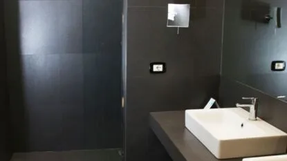 Bagno moderno con lavabo bianco rettangolare, rubinetto cromato e pareti nere.