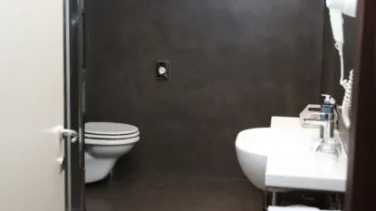Bagno moderno con pareti scure, wc sospeso bianco, lavabo bianco con rubinetto e asciugacapelli a parete.
