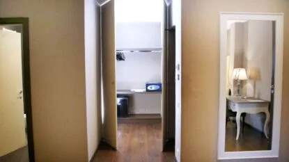 Corridoio con porta aperta su armadio con cassaforte e specchio che riflette una scrivania con lampada accesa.