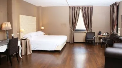 Camera d'albergo elegante con letto matrimoniale, poltrone nere, scrivania bianca e pavimento in legno scuro.