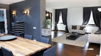 Soggiorno moderno con tavolo in legno, divani beige, tende scure e pavimento in legno lucido.
