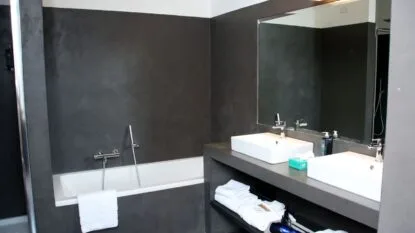 Bagno moderno con vasca bianca, doppio lavabo, specchio grande e pareti grigie scure.