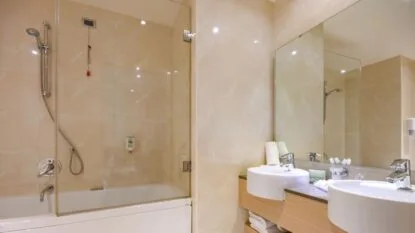 Bagno moderno con doccia a vetro, doppio lavabo e grande specchio.