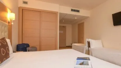 Camera d'albergo con letto matrimoniale, due letti singoli, armadio scorrevole e televisore a parete.