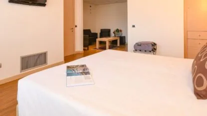 Camera d'albergo con letto matrimoniale, rivista aperta, due poltrone, tavolino e valigia su portavaligie.