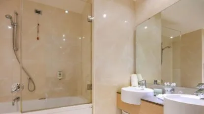 Bagno moderno con vasca e doccia a parete in vetro, lavabo doppio e grande specchio su parete beige.