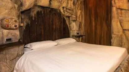 Camera con letto matrimoniale bianco e pareti che sembrano rocce, decorazioni rustiche in legno e luci soffuse.