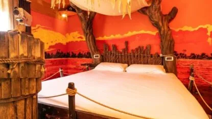 Camera con un letto dal design rustico, pareti rosse e decorazioni a tema naturale, illuminata da luci calde.