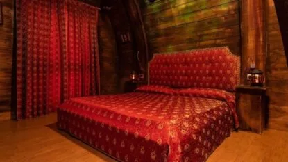 Camera da letto con pareti in legno scuro, letto matrimoniale con copriletto rosso e tende abbinate. Atmosfera accogliente.