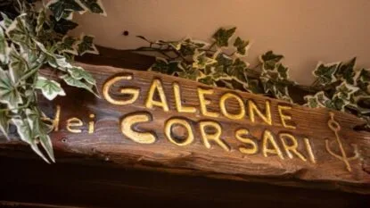 Insegna in legno con la scritta "Galeone dei Corsari", decorata con foglie di edera.
