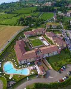 Complesso di edifici con piscina all'aperto, circondato da verde e campi coltivati, vista aerea in campagna.