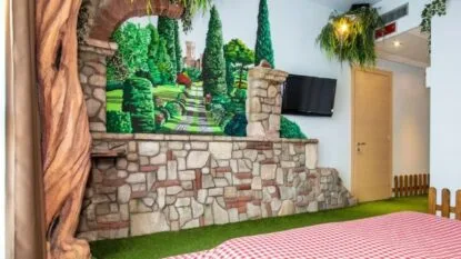 Camera con murales di un giardino, parete in pietra, TV e dettagli rustici come erba sintetica e una staccionata.