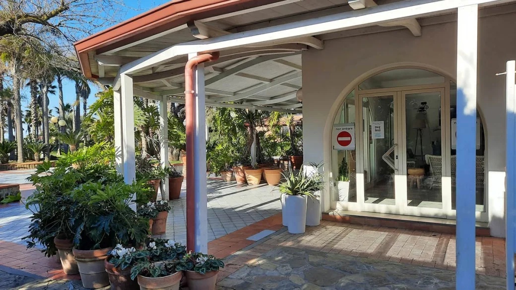 Ingresso della reception con tettoia in legno, piante in vaso e porta a vetri