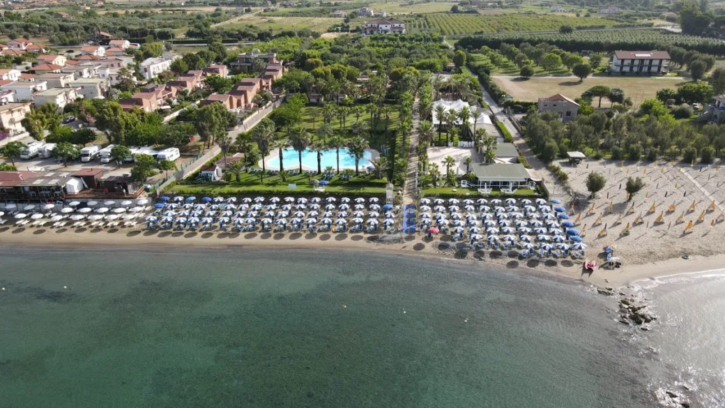 Veduta aerea del villaggio con piscina, spiaggia attrezzata e campagna circostante