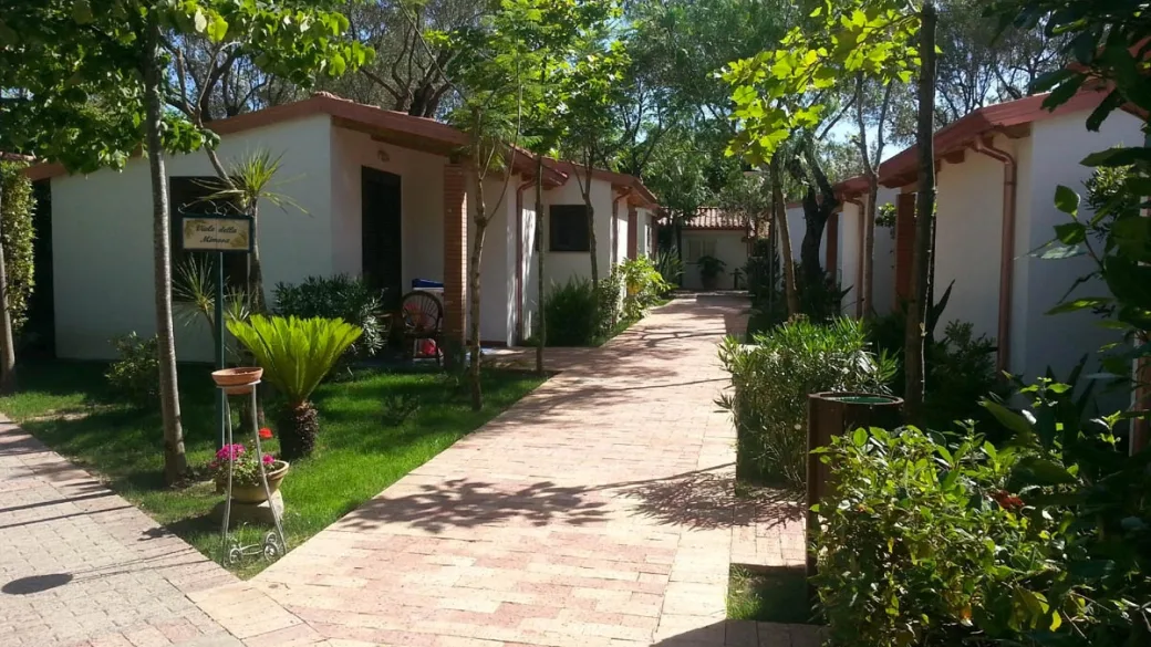 Vialetto pavimentato tra bungalow bianchi con giardini fioriti e vegetazione