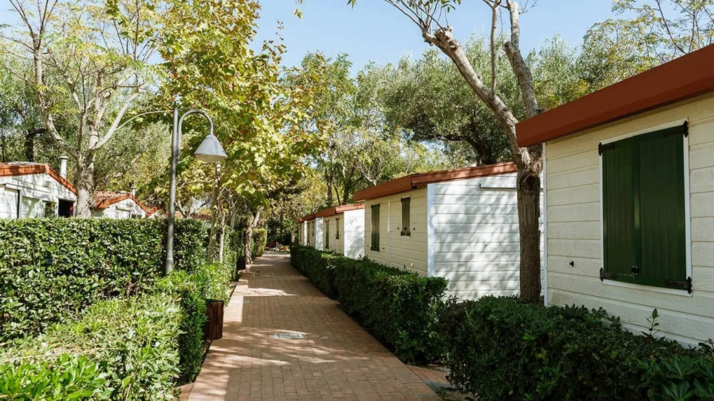 Sentiero pavimentato tra bungalow bianchi con persiane verdi e siepi curate