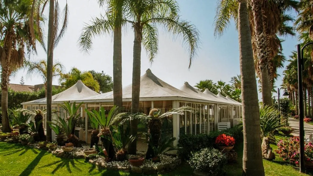 Struttura con tendoni bianchi circondata da palme e giardino fiorito