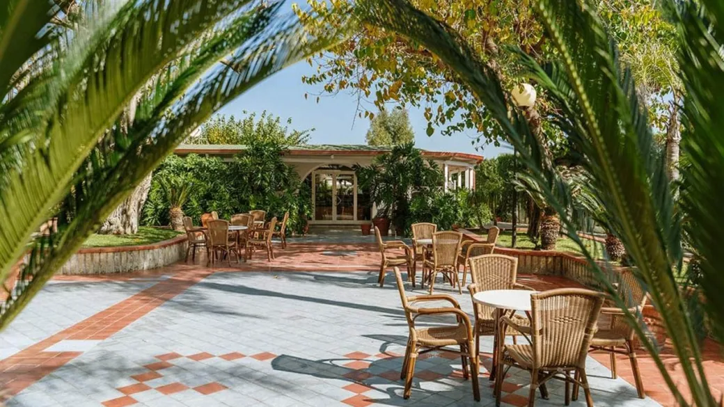 Terrazza esterna con tavolini e sedie in vimini circondata da vegetazione tropicale