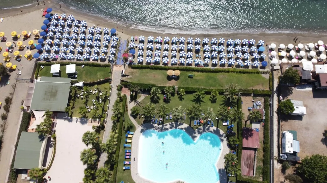 Vista aerea della spiaggia con ombrelloni, giardino e piscina del villaggio