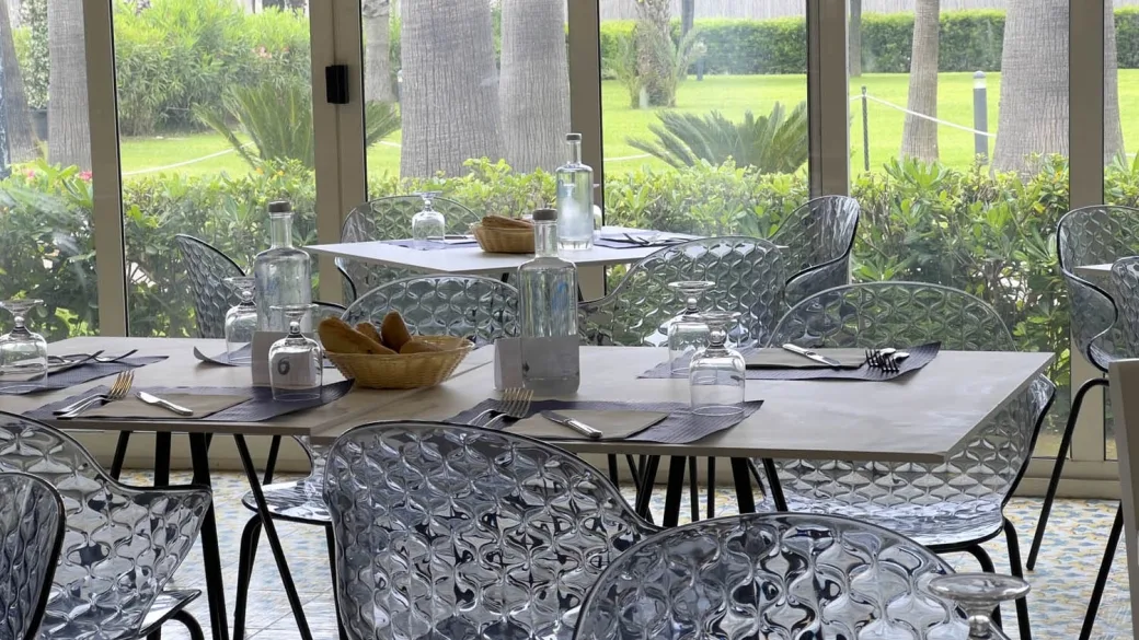 Sala ristorante interna con sedie trasparenti e tavoli apparecchiati affacciata sul giardino
