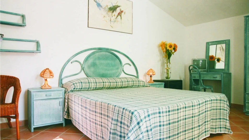 Camera matrimoniale con arredi verdi in vimini, letto a quadri e specchiera