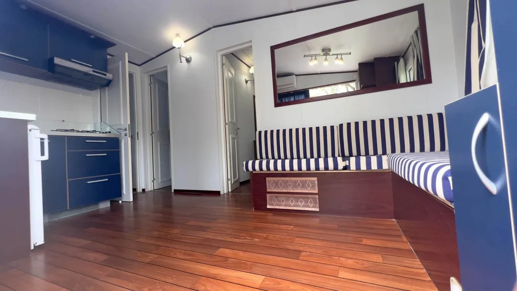 Interno di mobile home con cucina blu, divano a righe e pavimento in legno