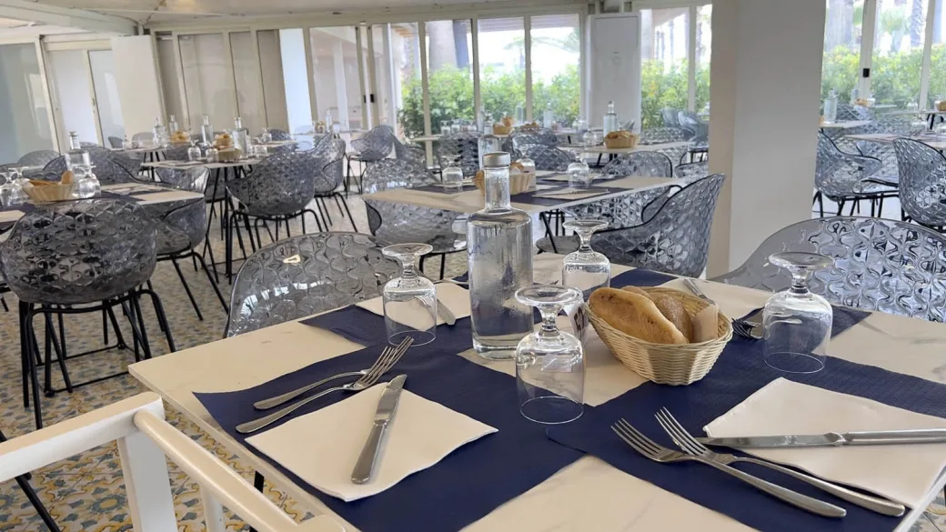Sala ristorante con tavoli apparecchiati, sedie trasparenti e tovaglie blu